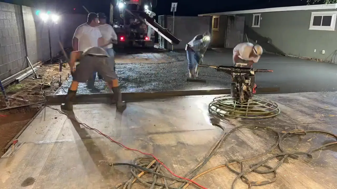 Crew screeding and power troweling a concrete slab during a night pour